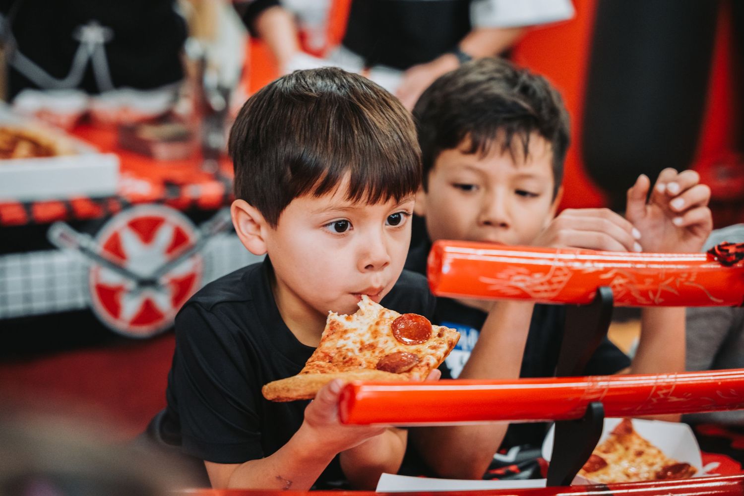 Young students eating pizza from red trays during a martial arts studio celebration.