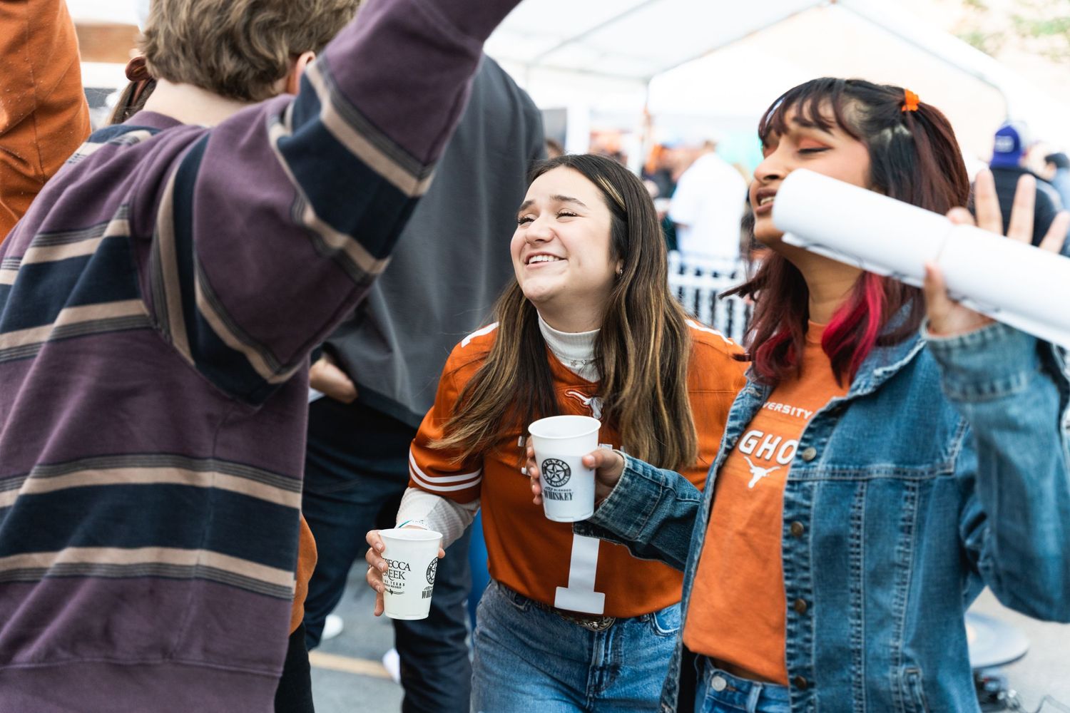 Students sharing laughter while holding drinks at an outdoor university gathering.