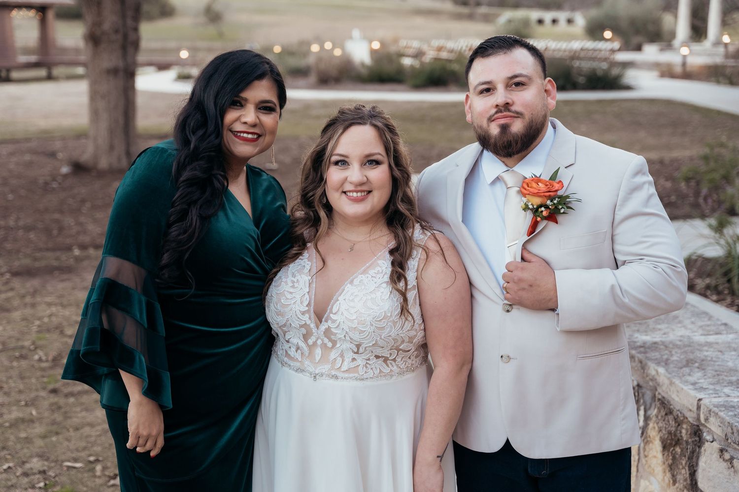 Three people pose together at an outdoor wedding venue.