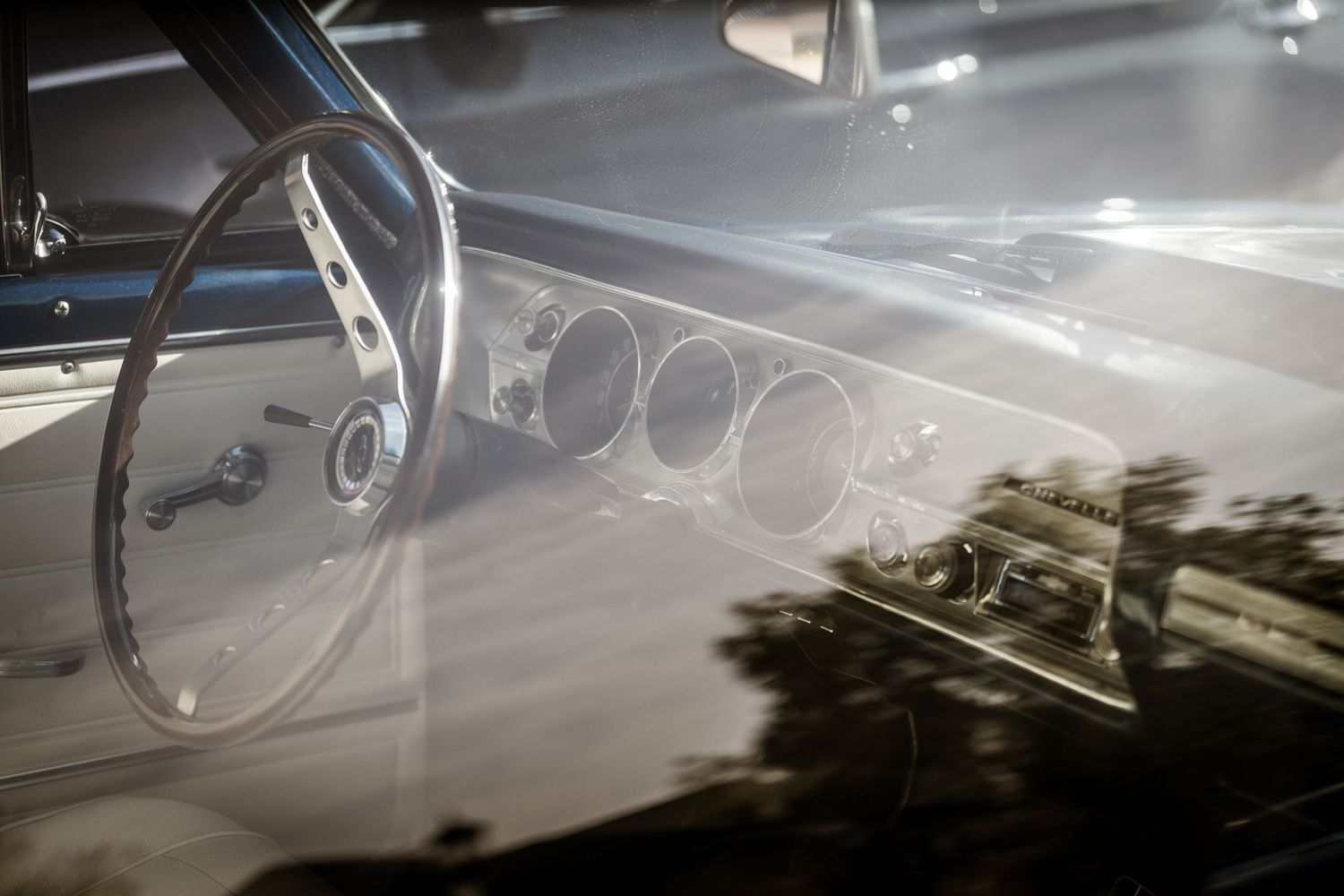 Interior dashboard view of a classic car showing steering wheel and gauge cluster through windshield.