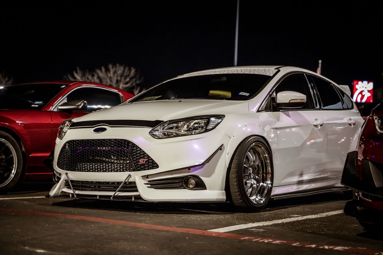 Lowered white Ford Focus ST with custom wheels and body modifications at a car show.