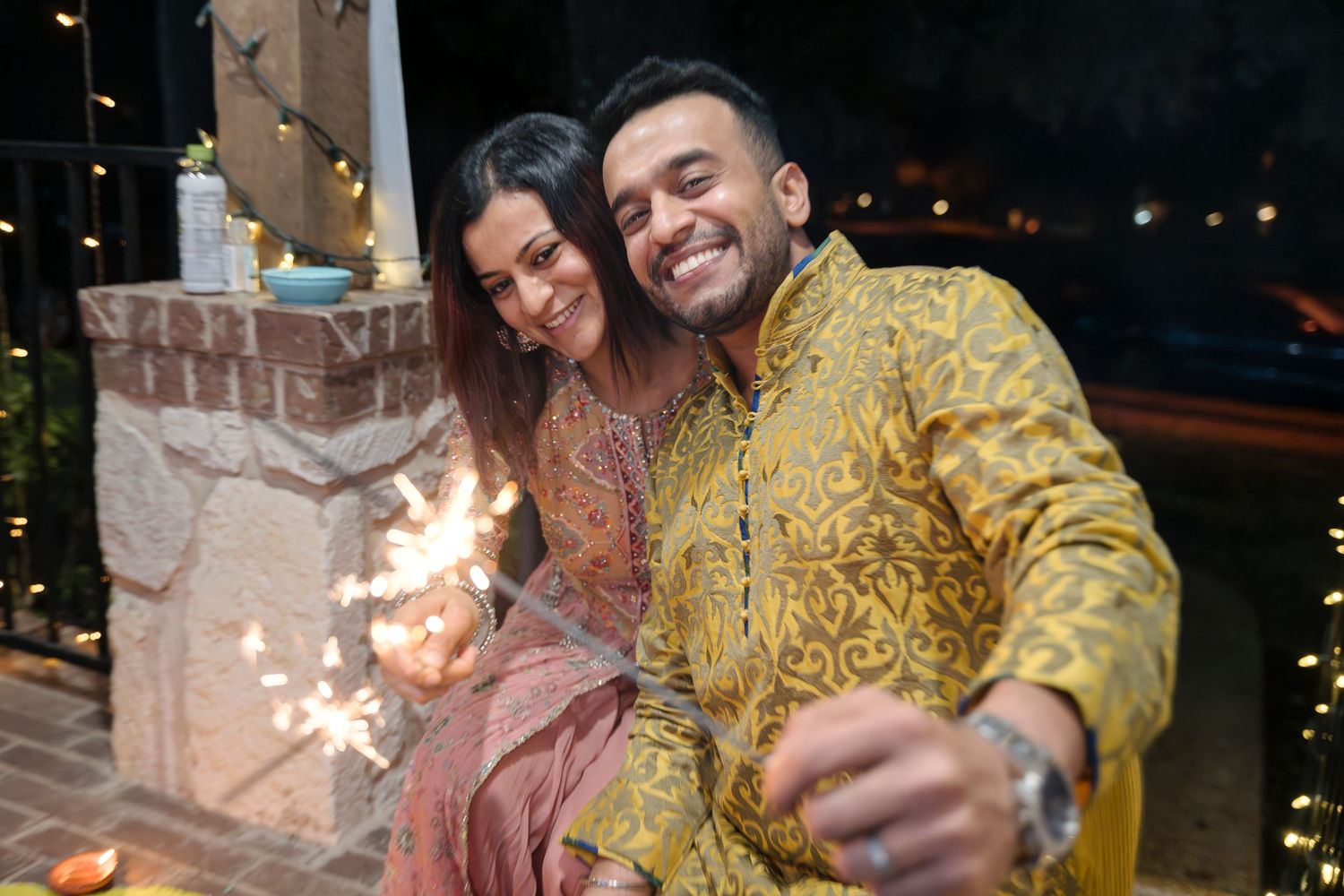 Couple in festive attire holding sparklers during a nighttime celebration.