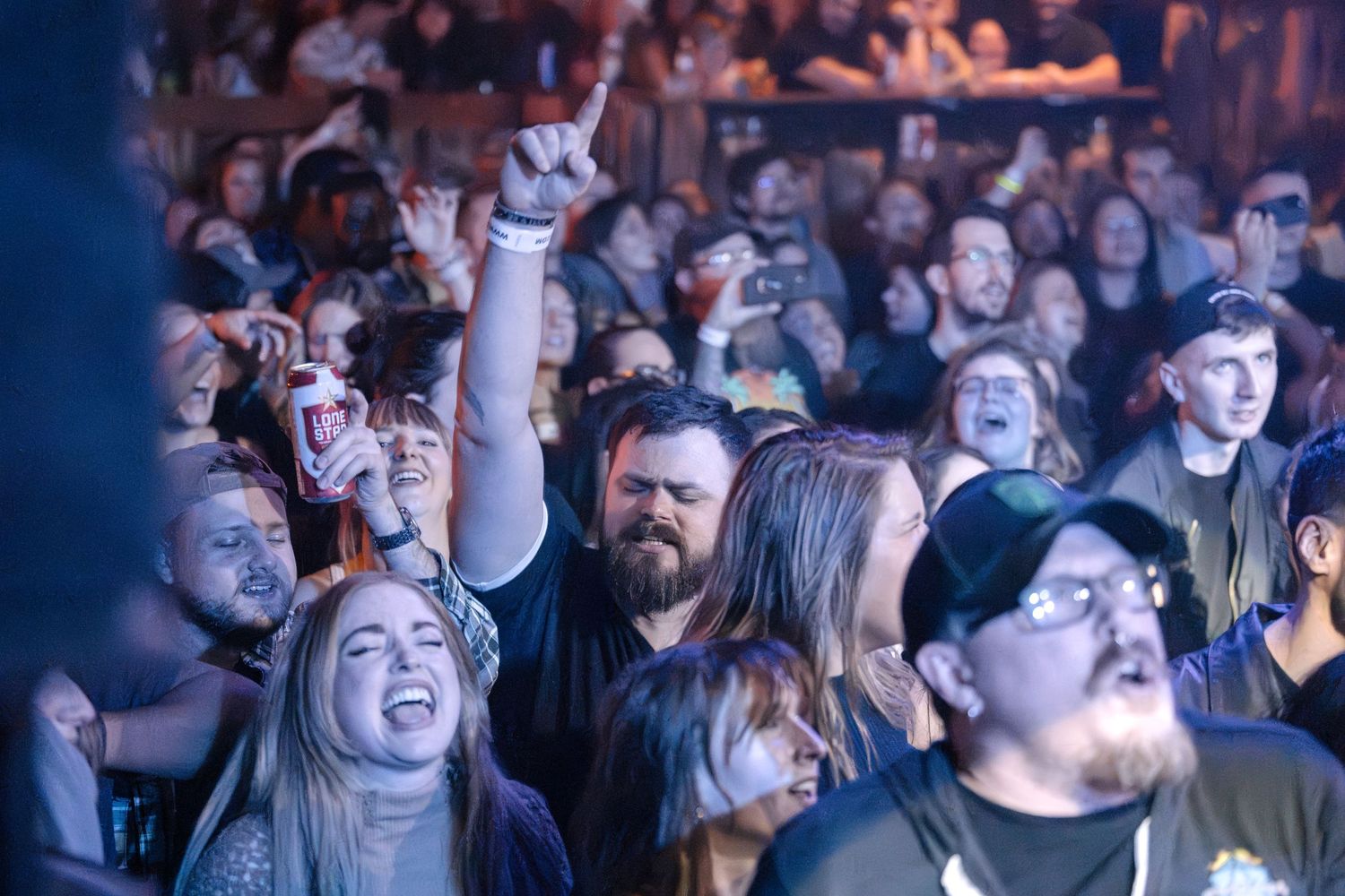 Enthusiastic crowd enjoying live music at a concert venue with hands raised and excited expressions.