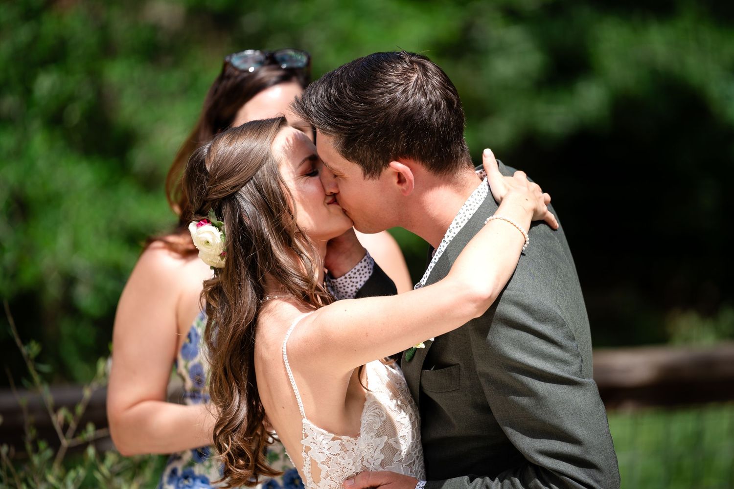 A romantic kiss between newlyweds surrounded by lush greenery during an outdoor wedding ceremony.