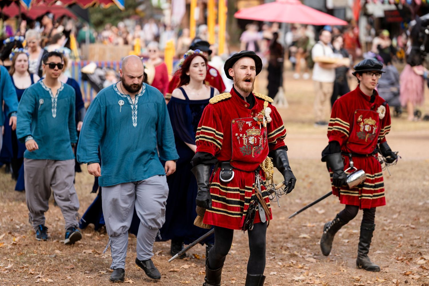 Group of people in medieval costumes and red cloaks walking together at a renaissance festival.