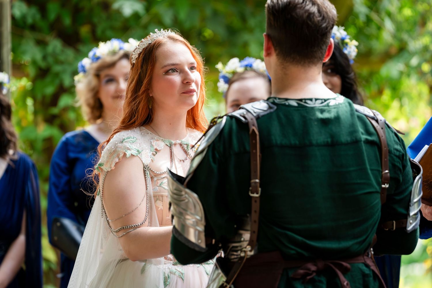 A couple in wedding attire dances together outdoors surrounded by greenery and guests.