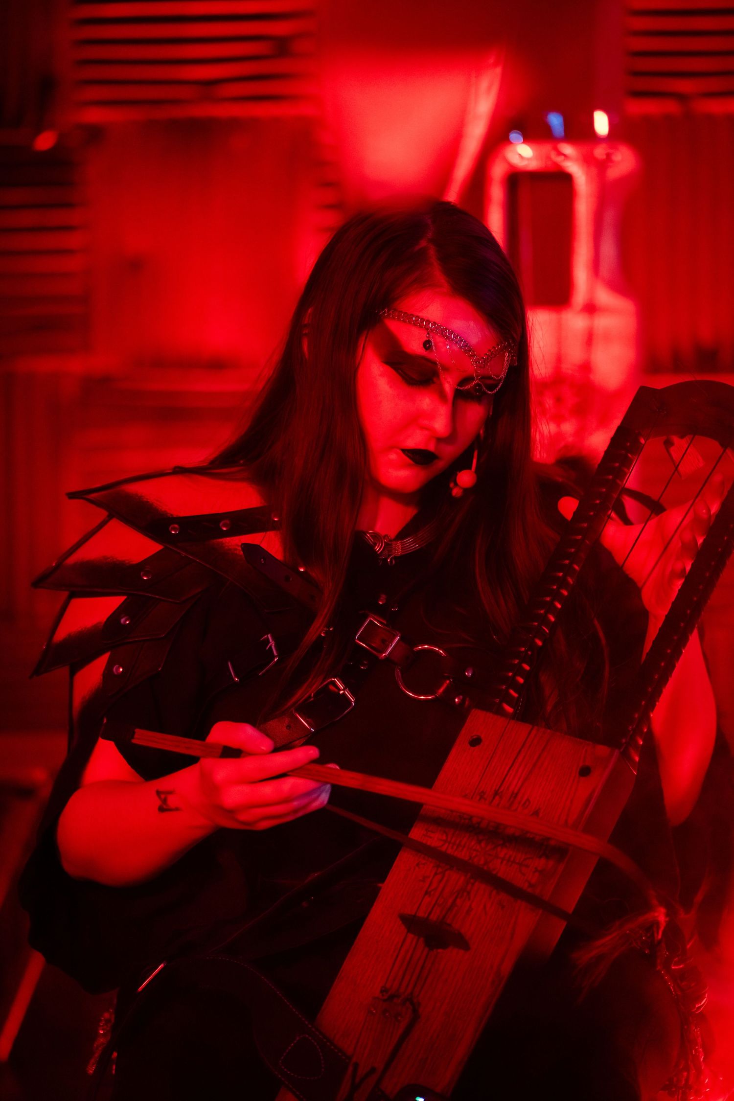 Dark atmospheric photo of a musician in gothic attire bathed in red light holding an instrument.
