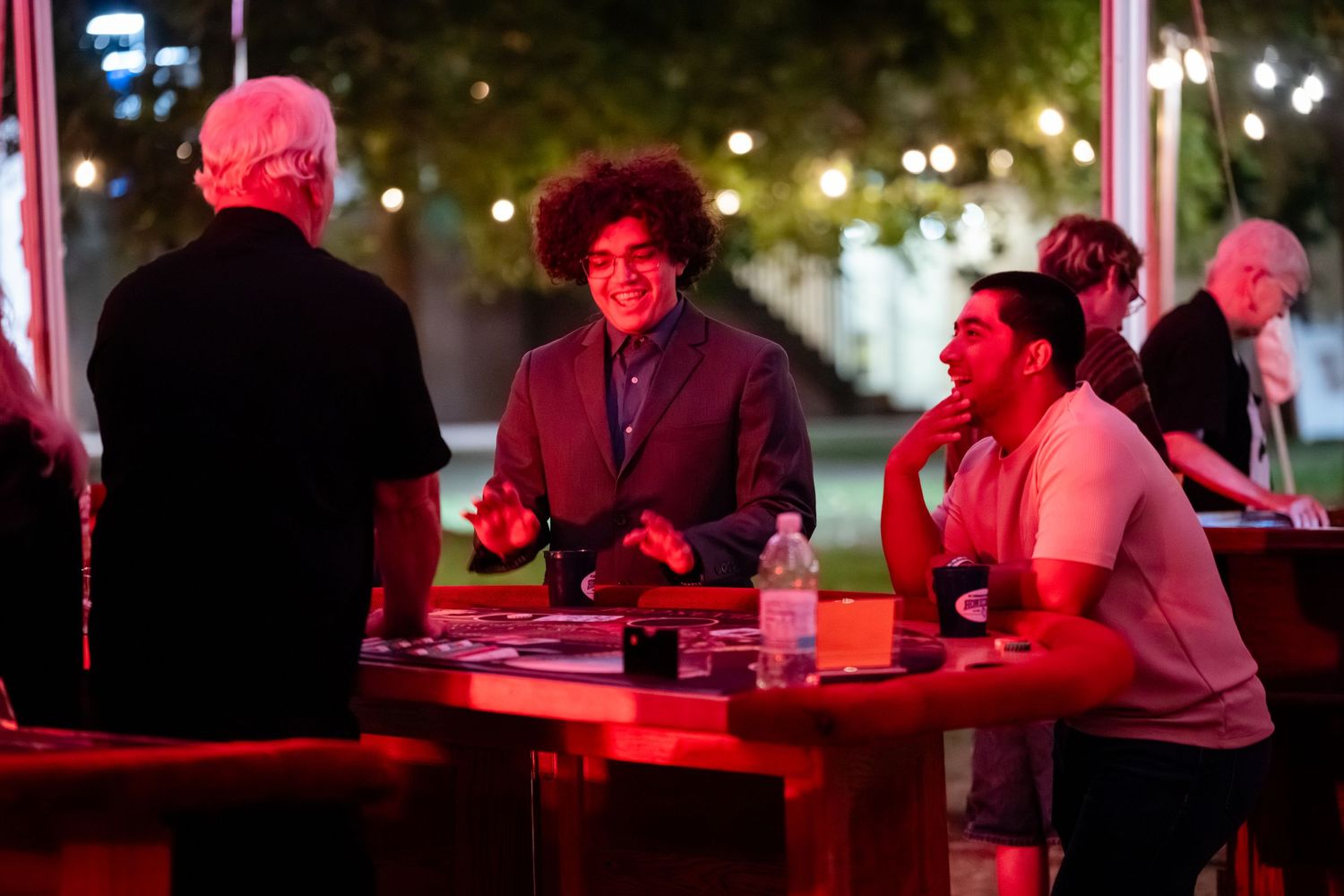 People sit at a table illuminated by red lighting during an outdoor nighttime gathering.