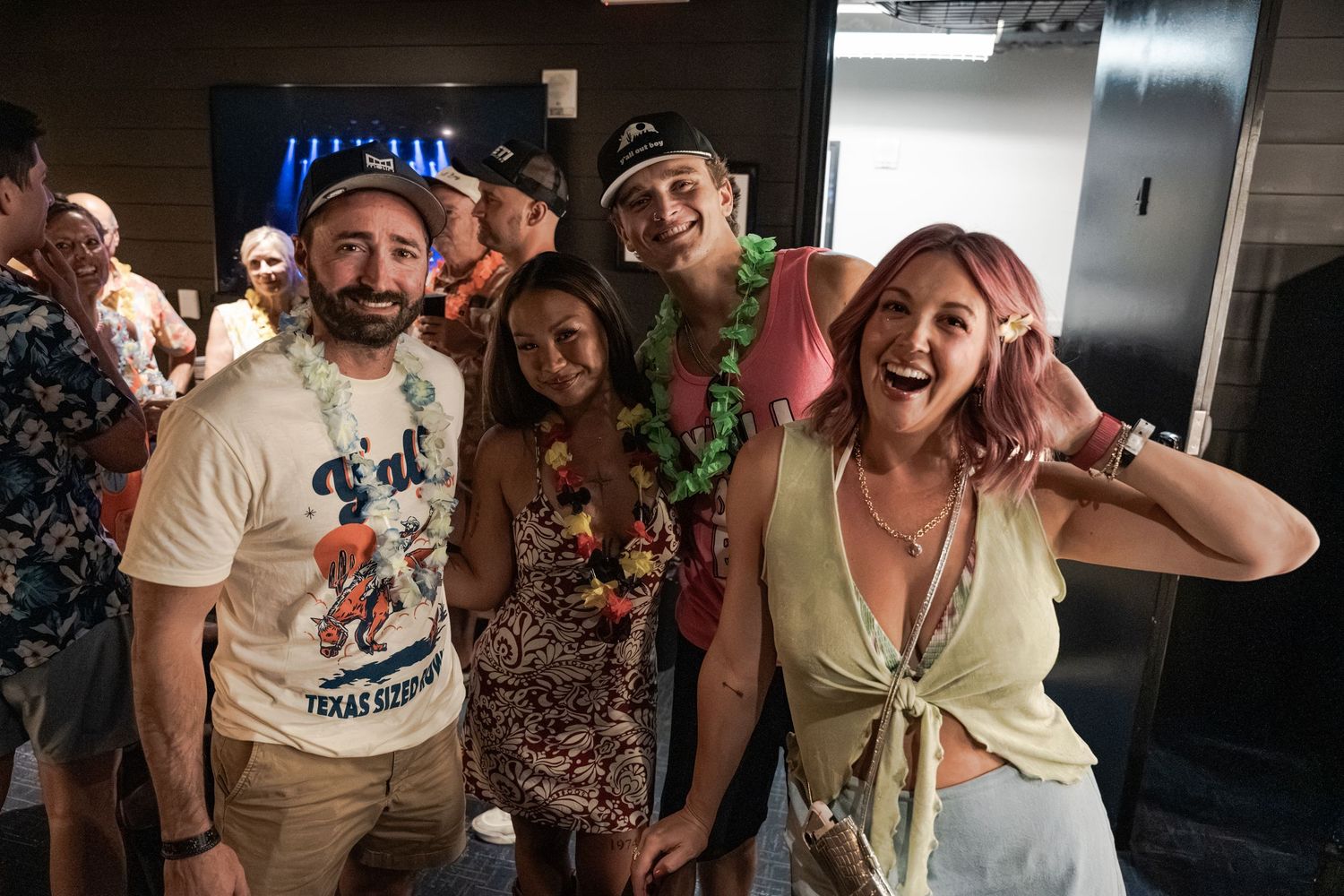 Group of friends posing and smiling at a tropical-themed party, wearing leis and colorful outfits.