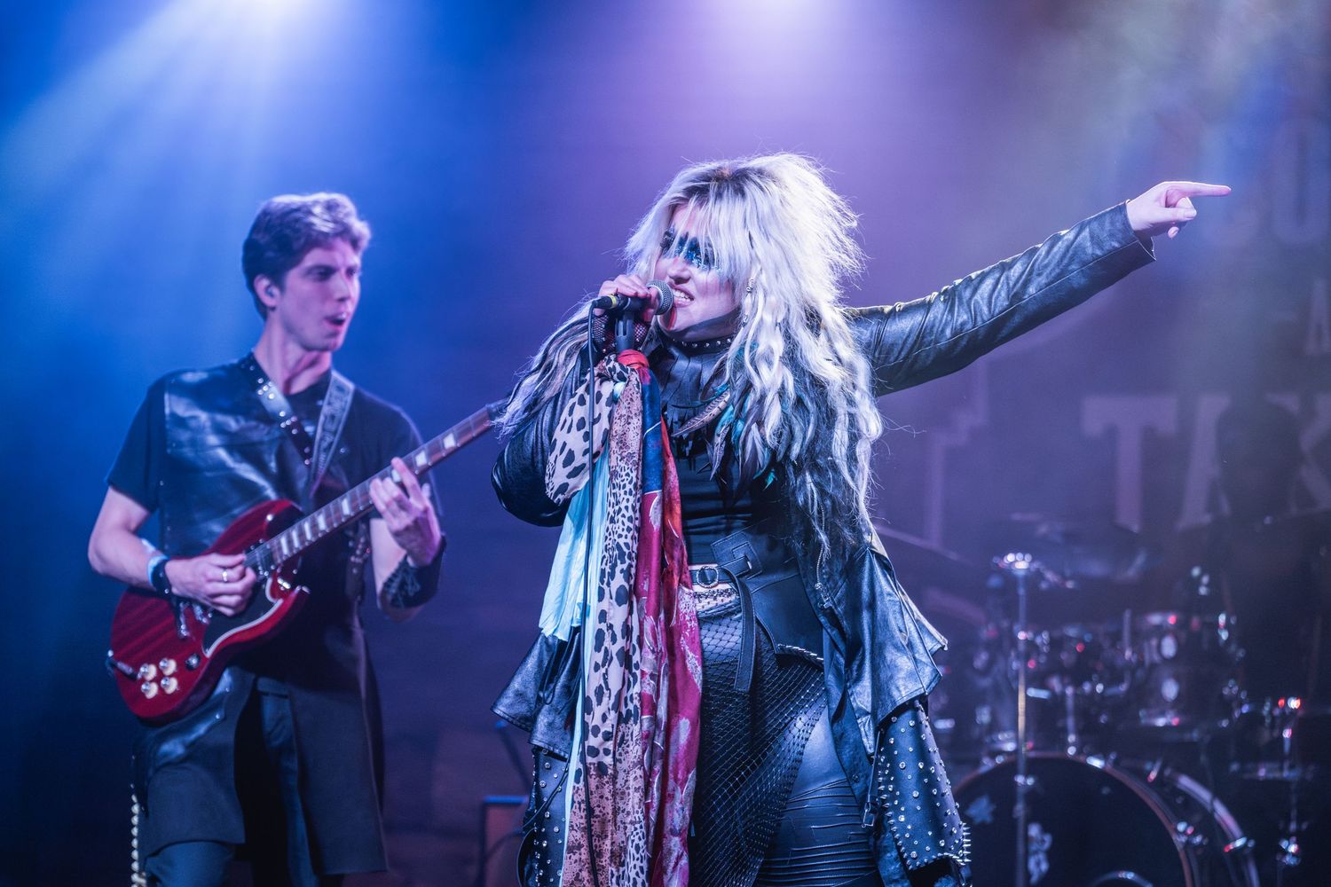 Energetic rock band performs on stage with dramatic blue lighting and smoke effects during a live concert performance.