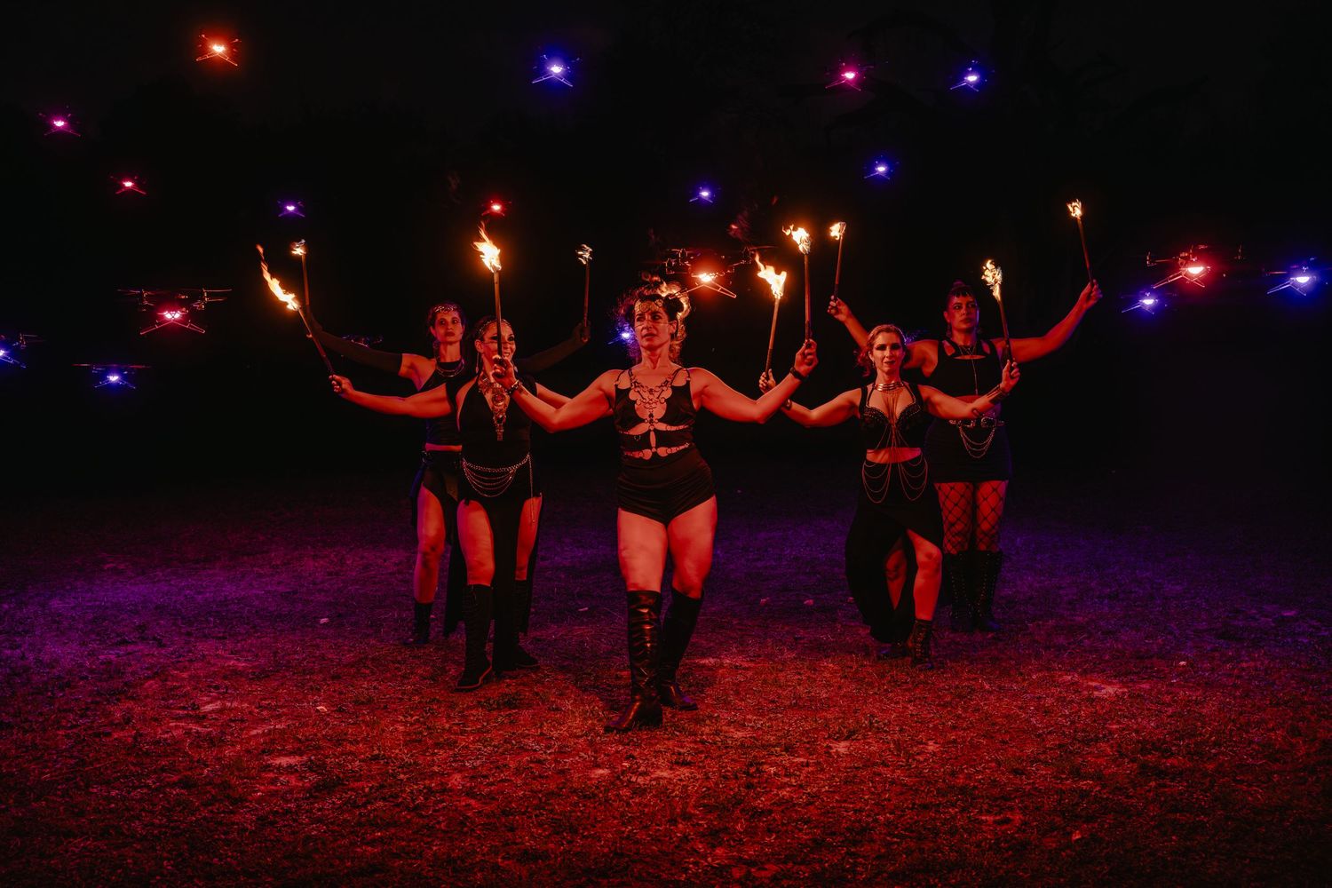 Fire dancers perform at night, holding torches under colorful lights in a dramatic outdoor show.