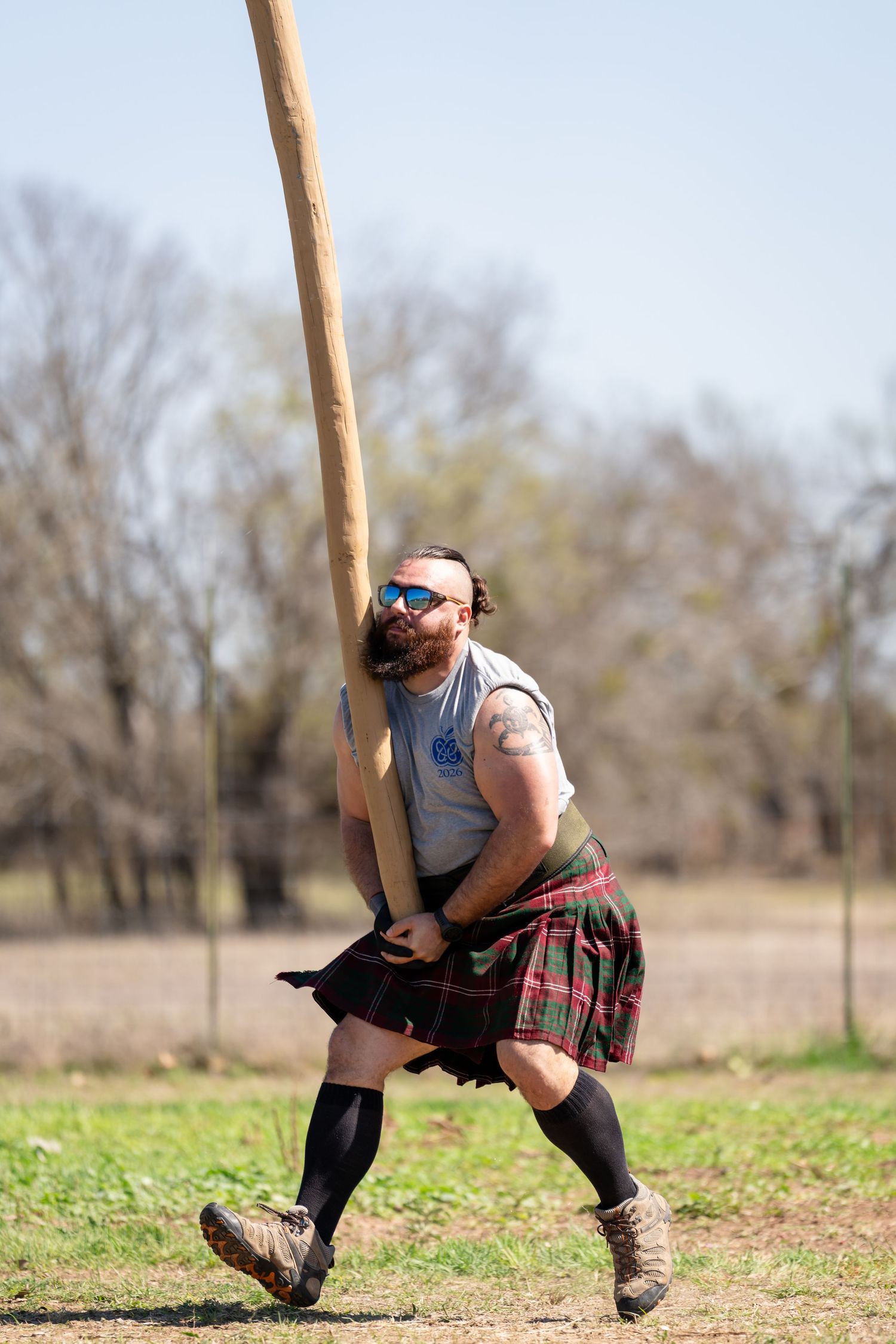 Man in tartan kilt tossing a caber at a Highland Games competition outdoors.