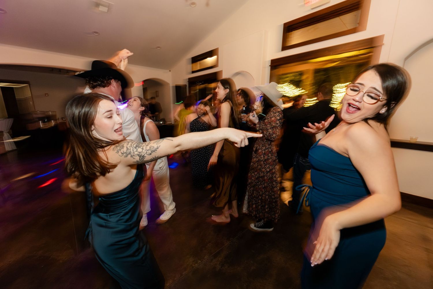 Women in elegant teal gowns dancing energetically at a lively wedding reception party.