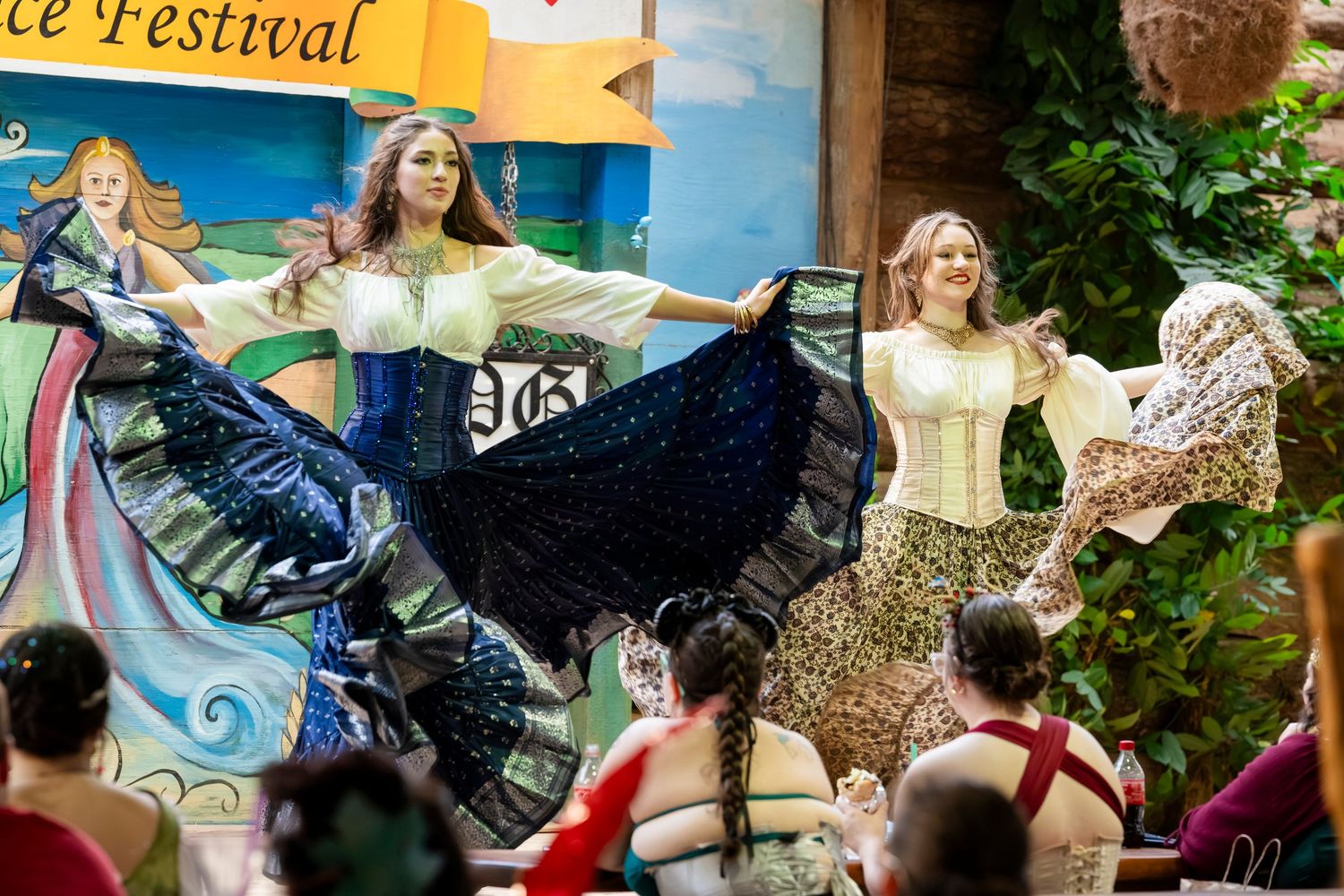Performers in flowing costumes dance and twirl during a Renaissance festival entertainment show.