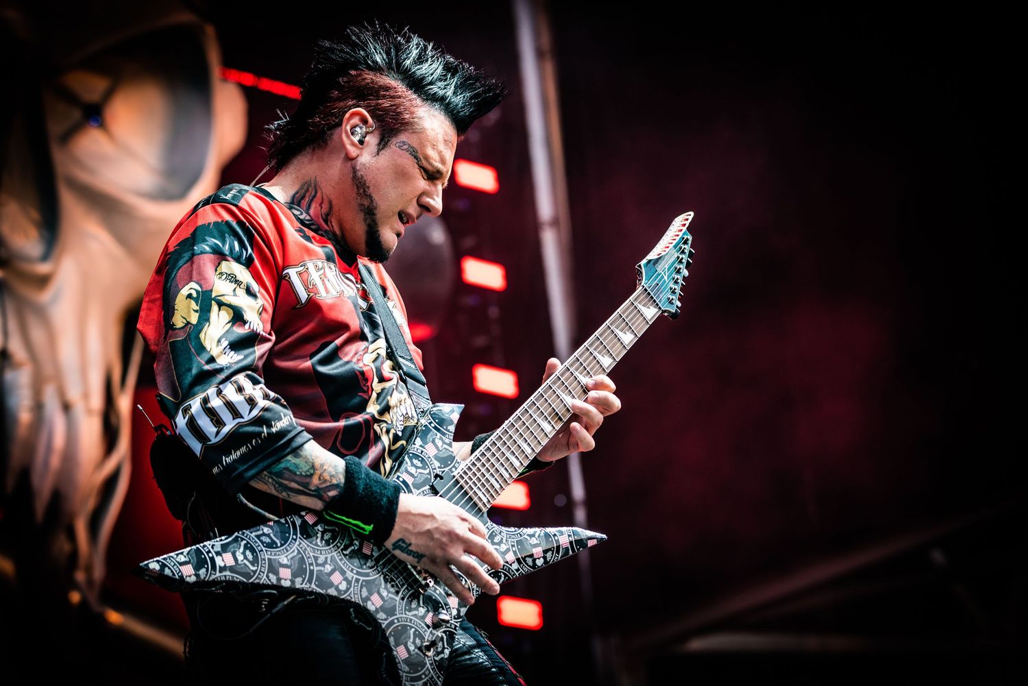 Heavy metal guitarist performs on stage with a custom patterned electric guitar under dramatic red lighting.