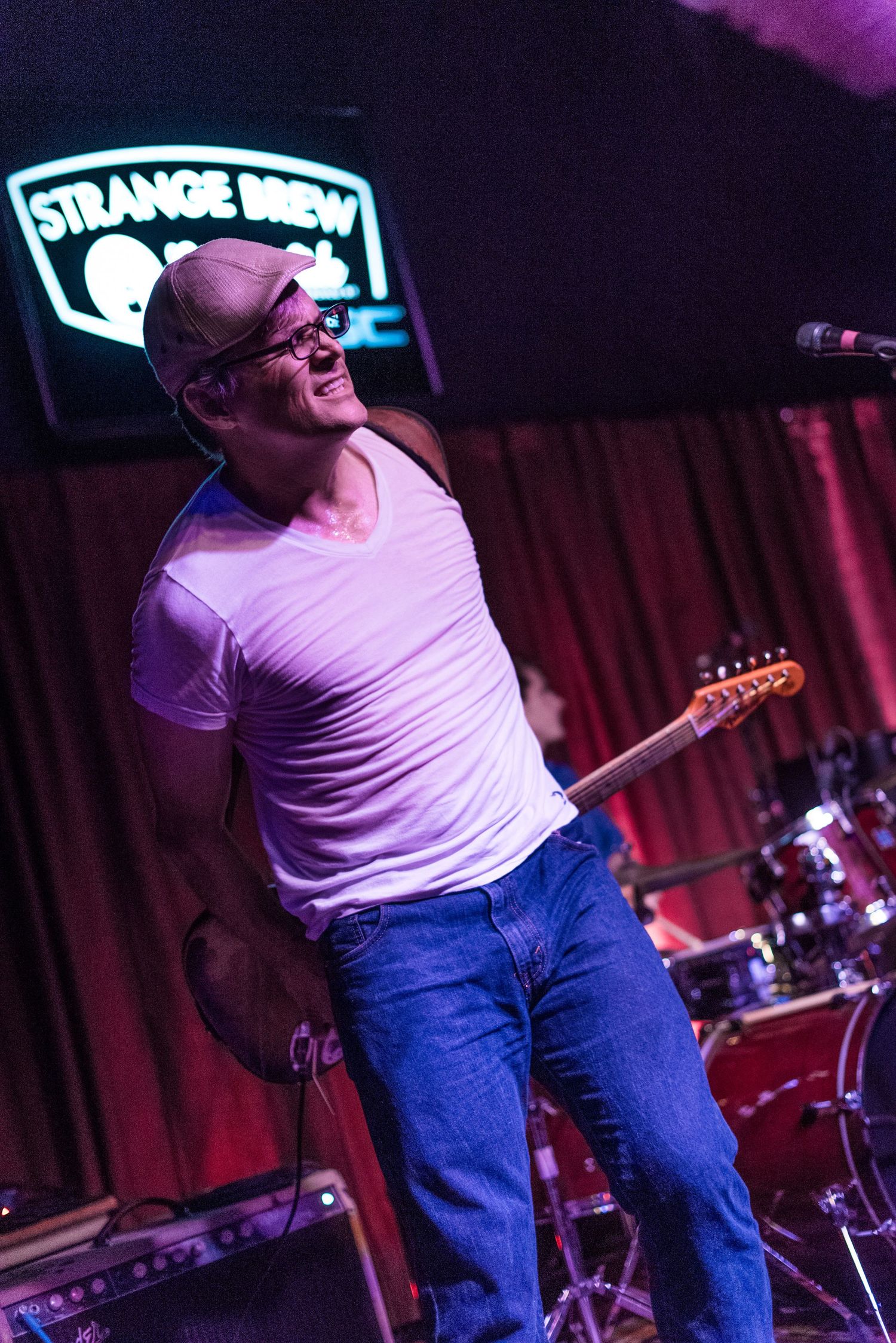 Guitarist performs energetically on stage at Strange Brew venue under purple lighting.