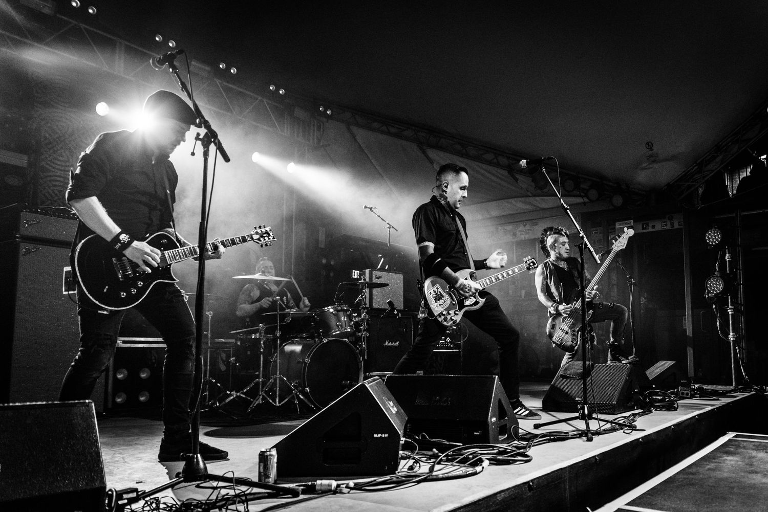 Black and white photo of a rock band performing on stage with dramatic backlighting and silhouetted musicians playing instruments.