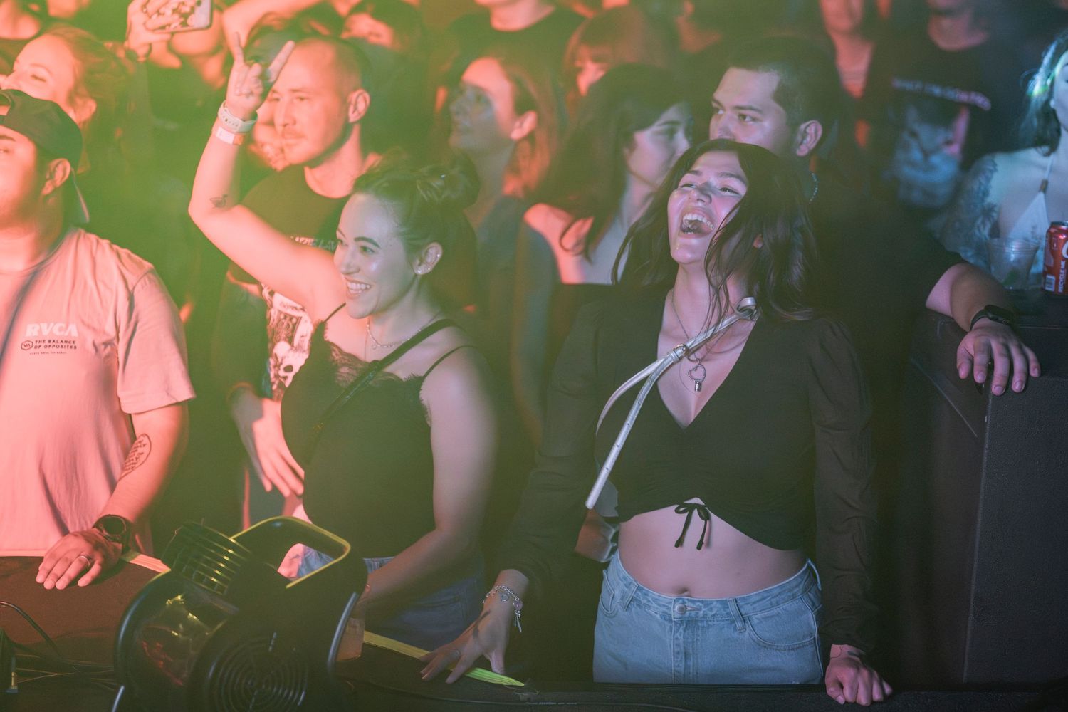 Concert crowd enjoying a live music performance in a dimly lit venue with pink and red lighting effects.