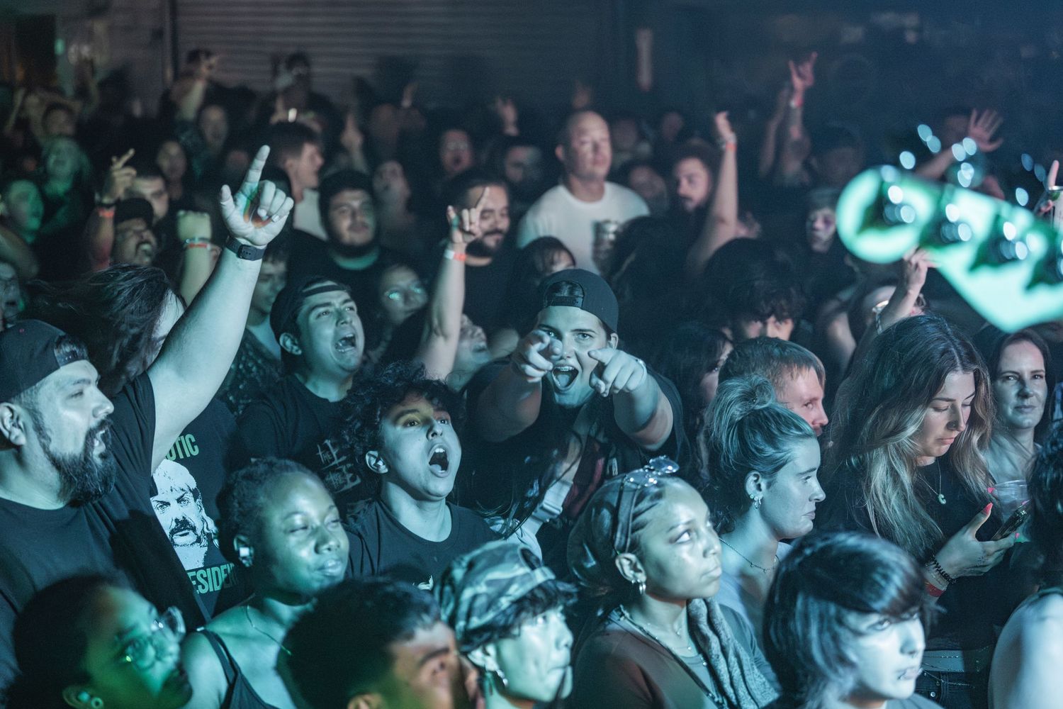 Energetic crowd of concert attendees reacting enthusiastically with raised arms and excited expressions in dark venue.
