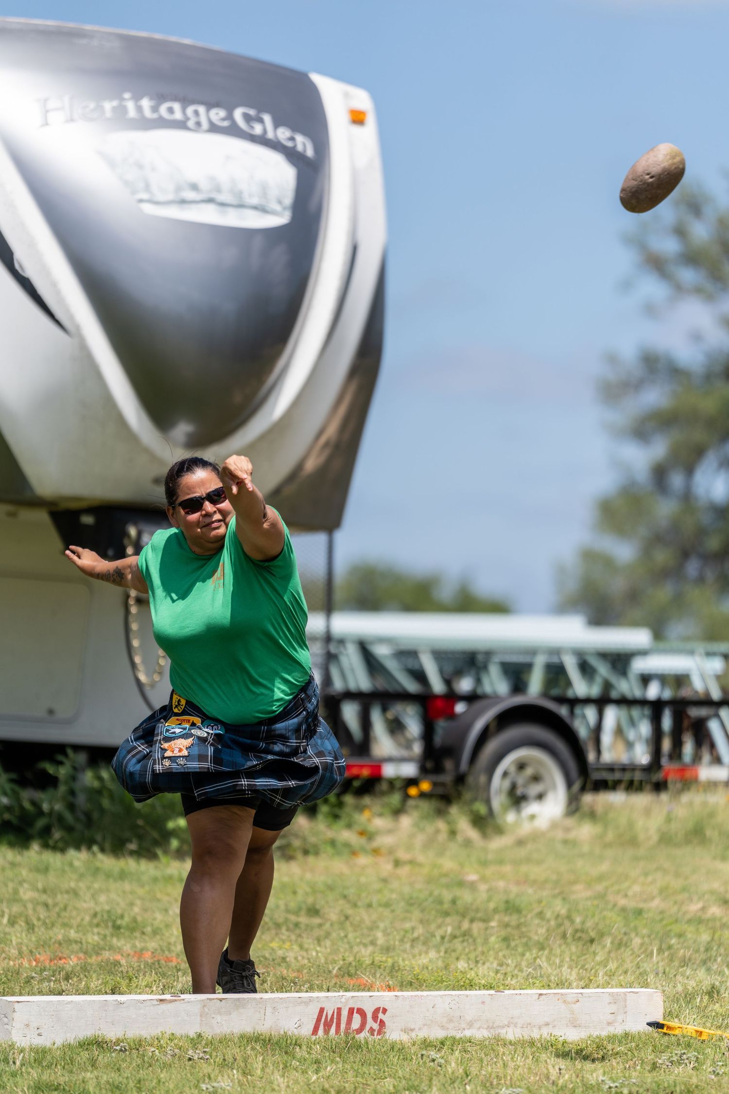 Woman in green shirt and kilt throws a stone at a Highland Games competition near a Heritage Glen RV.
