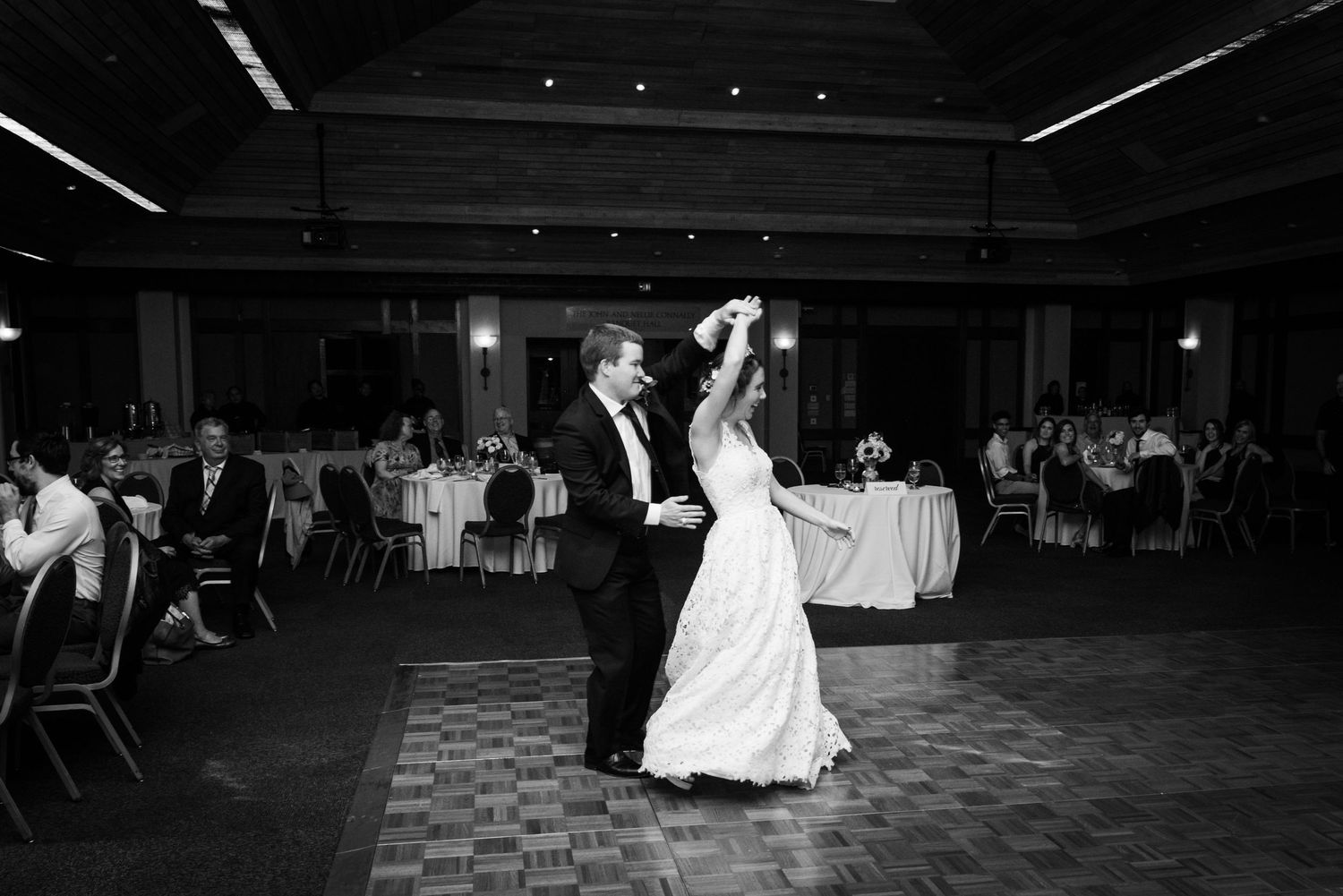 A couple shares their first dance at a wedding reception on a checkered dance floor in black and white.