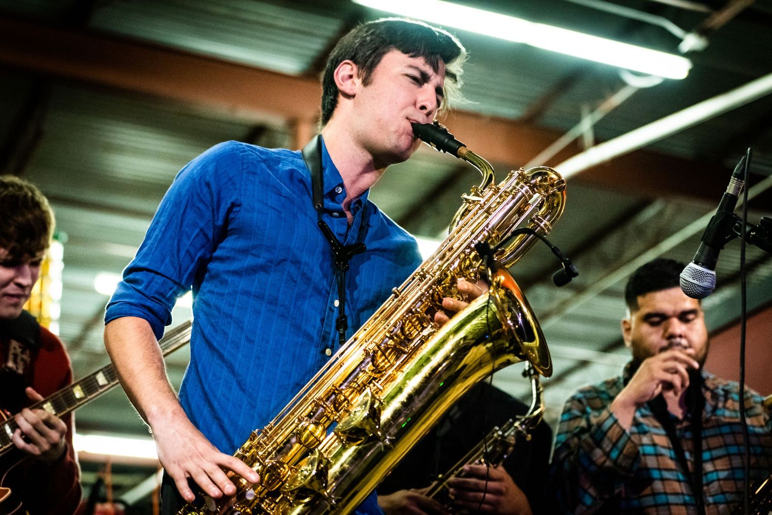 Musician in blue shirt plays saxophone with intense focus during performance.