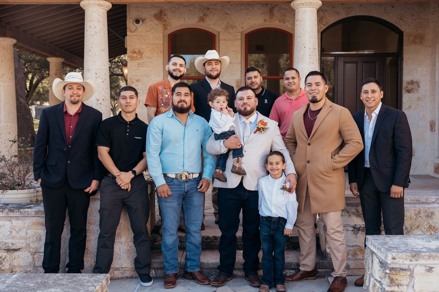 Group of formally dressed wedding guests posing together on stone steps.