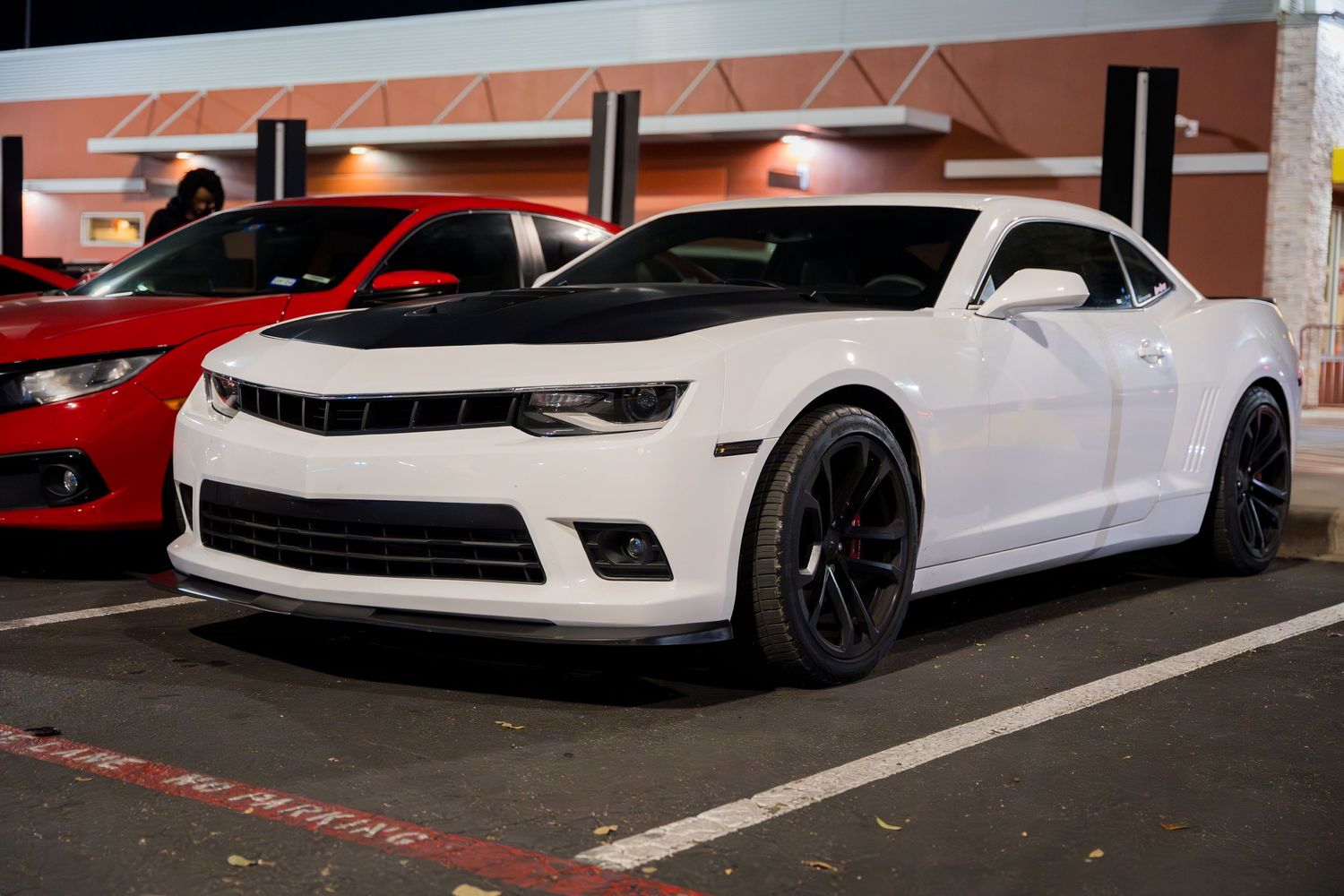 A white Chevrolet Camaro with black wheels parked at night.