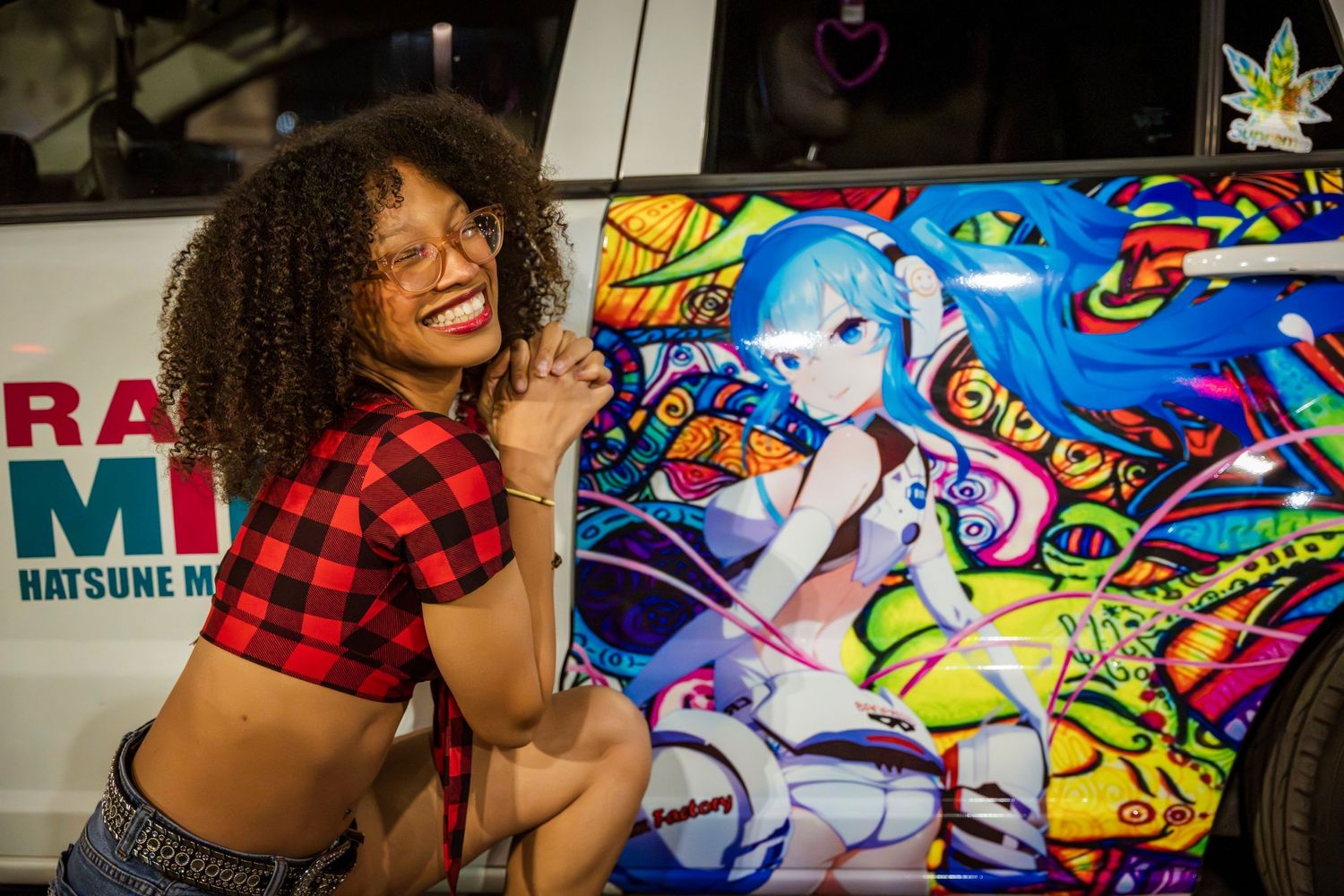 Woman poses next to car decorated with colorful anime-style artwork.
