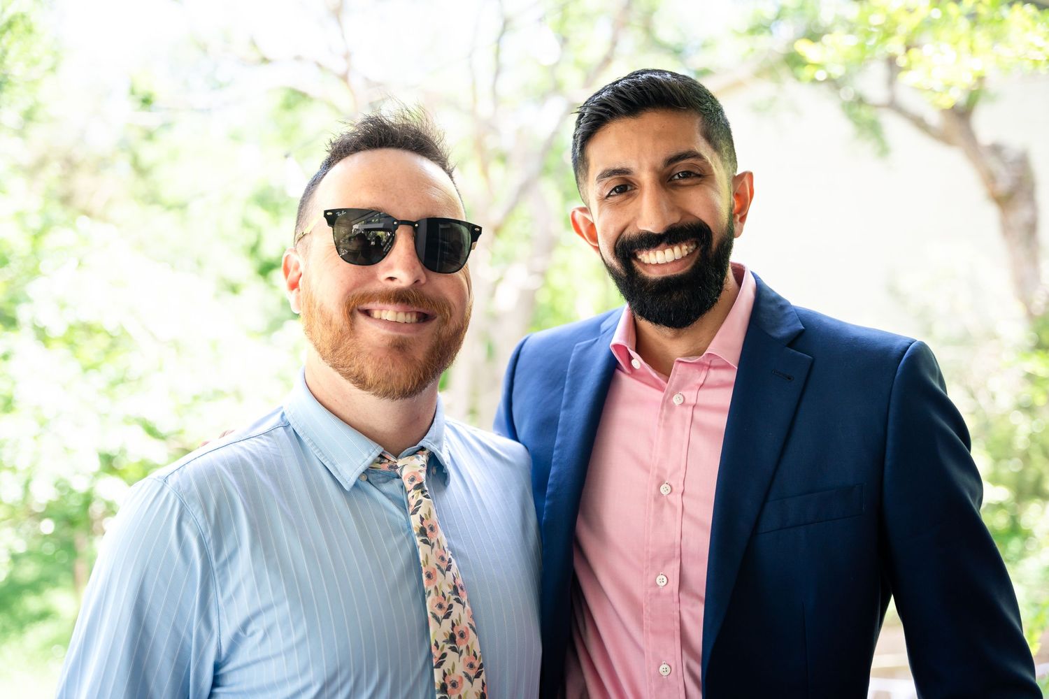 Two wedding guests in smart attire pose together at an outdoor celebration.