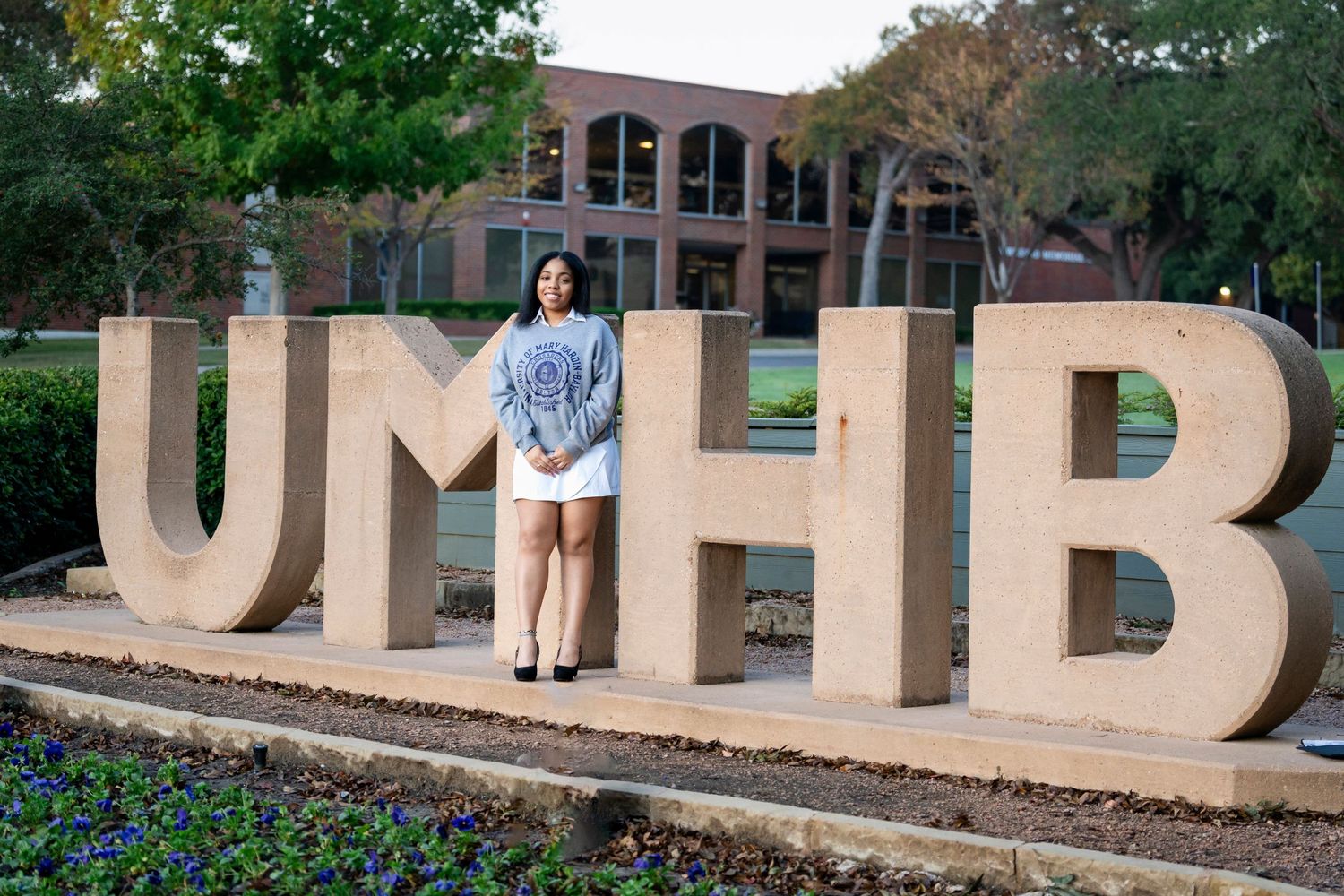 Graduate posing in front of large UMHB letters on campus during graduation photoshoot.