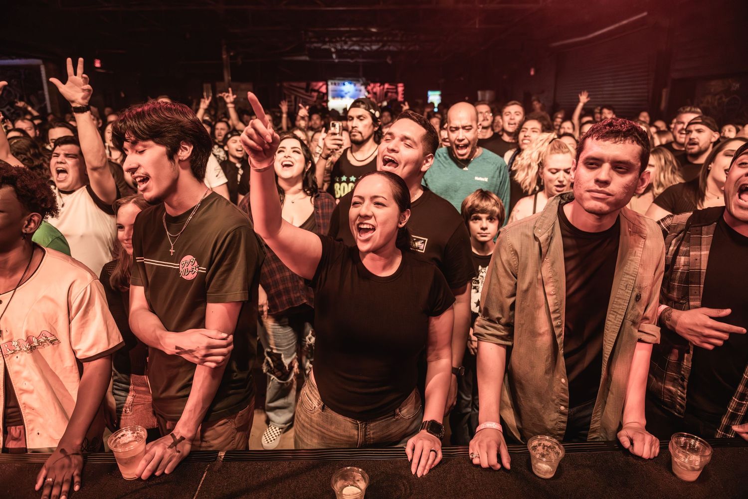 Enthusiastic concert crowd cheering and singing along during live music performance.