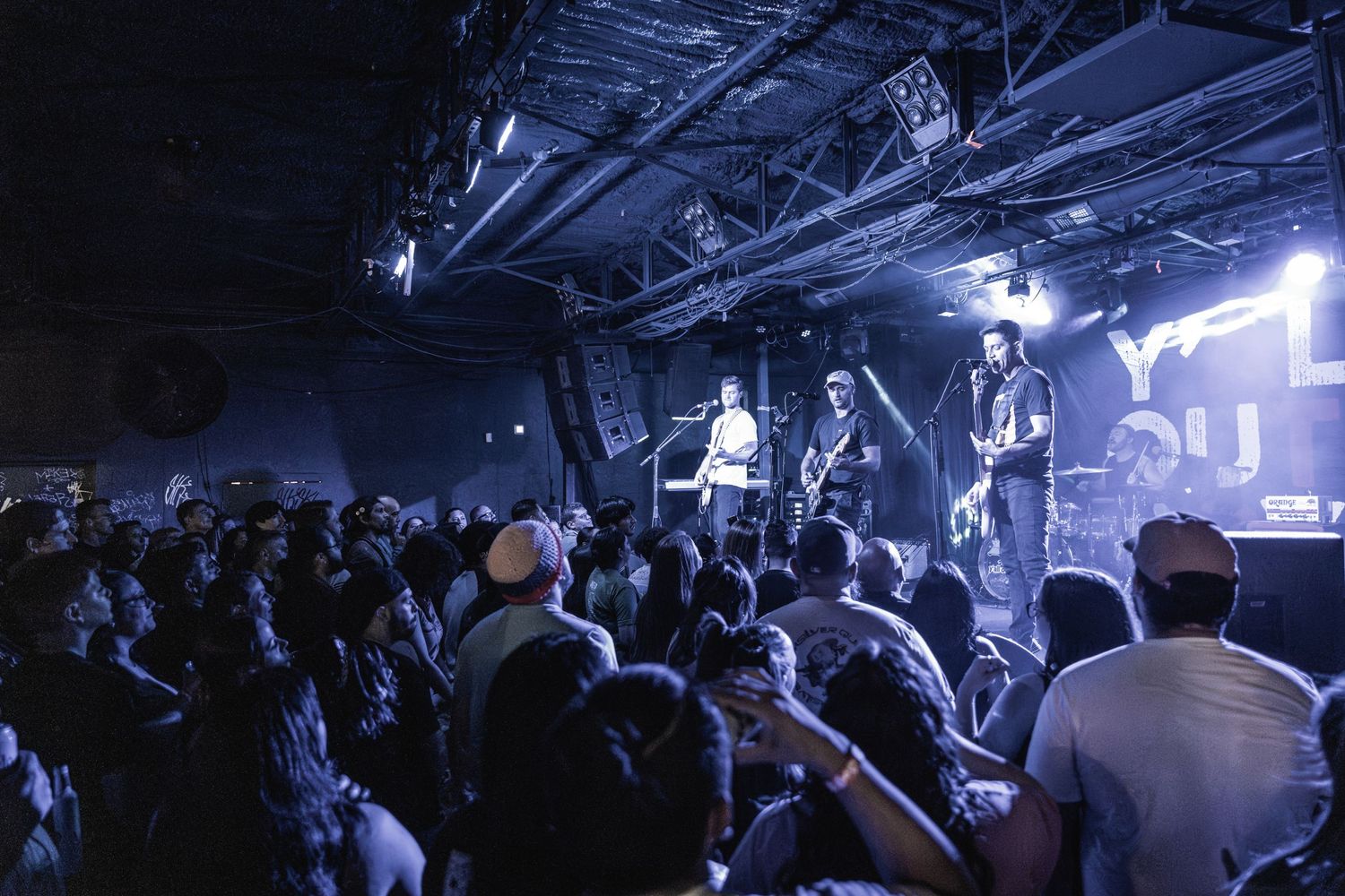 Energetic live music performance with crowd watching band on elevated stage under blue lights.
