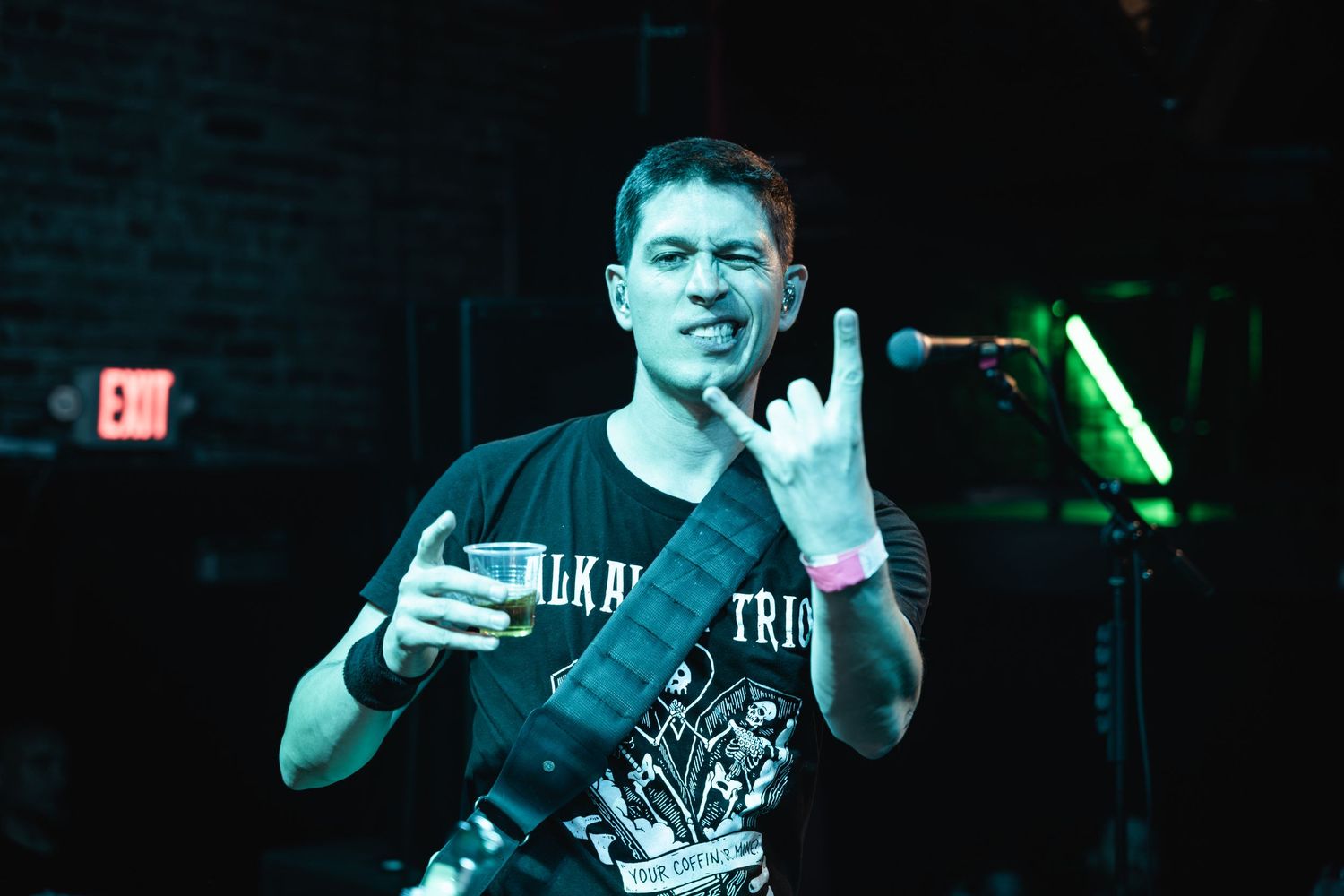 Rock musician gesturing while holding drink during stage performance.