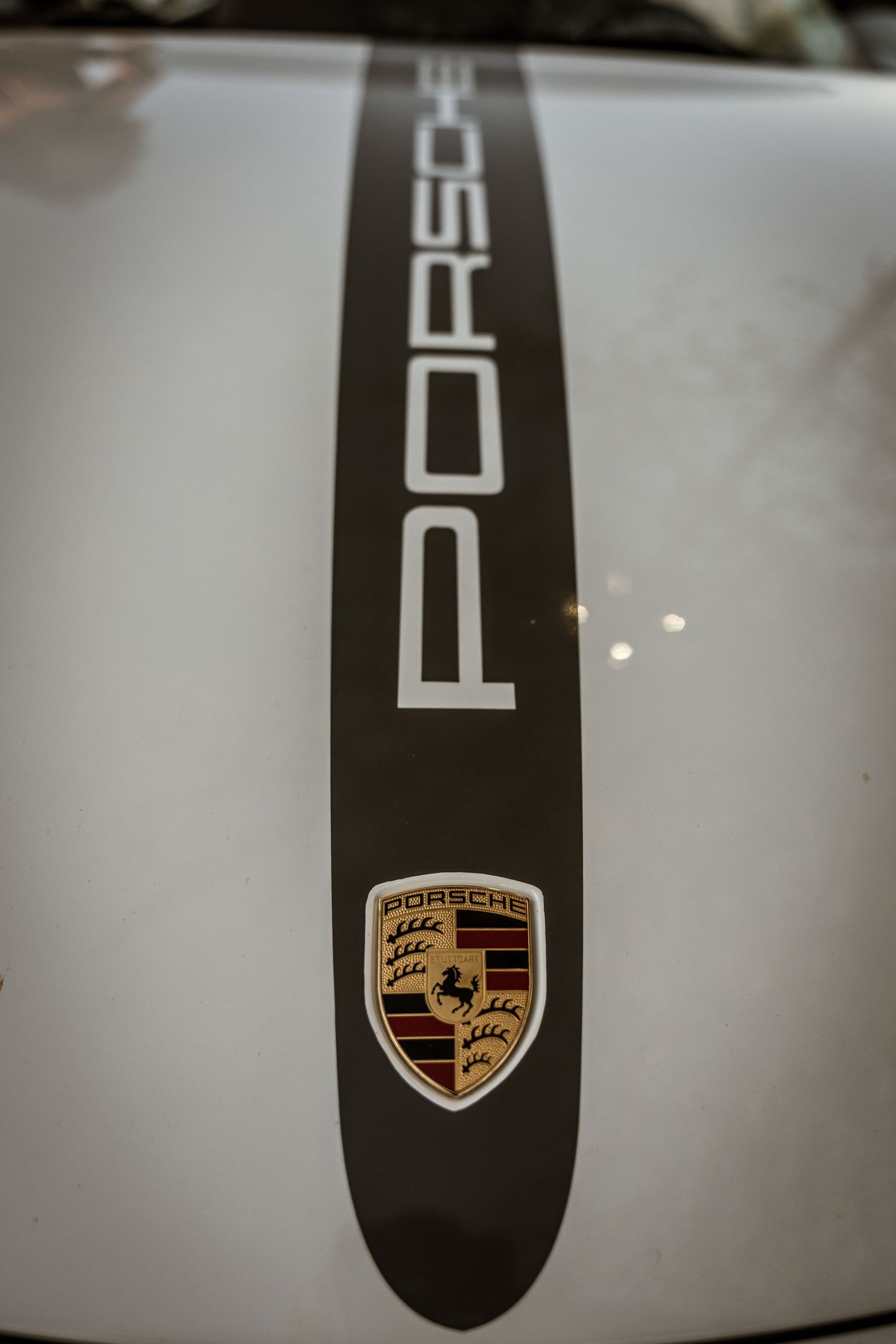 Close-up of Porsche logo and text on white car hood.