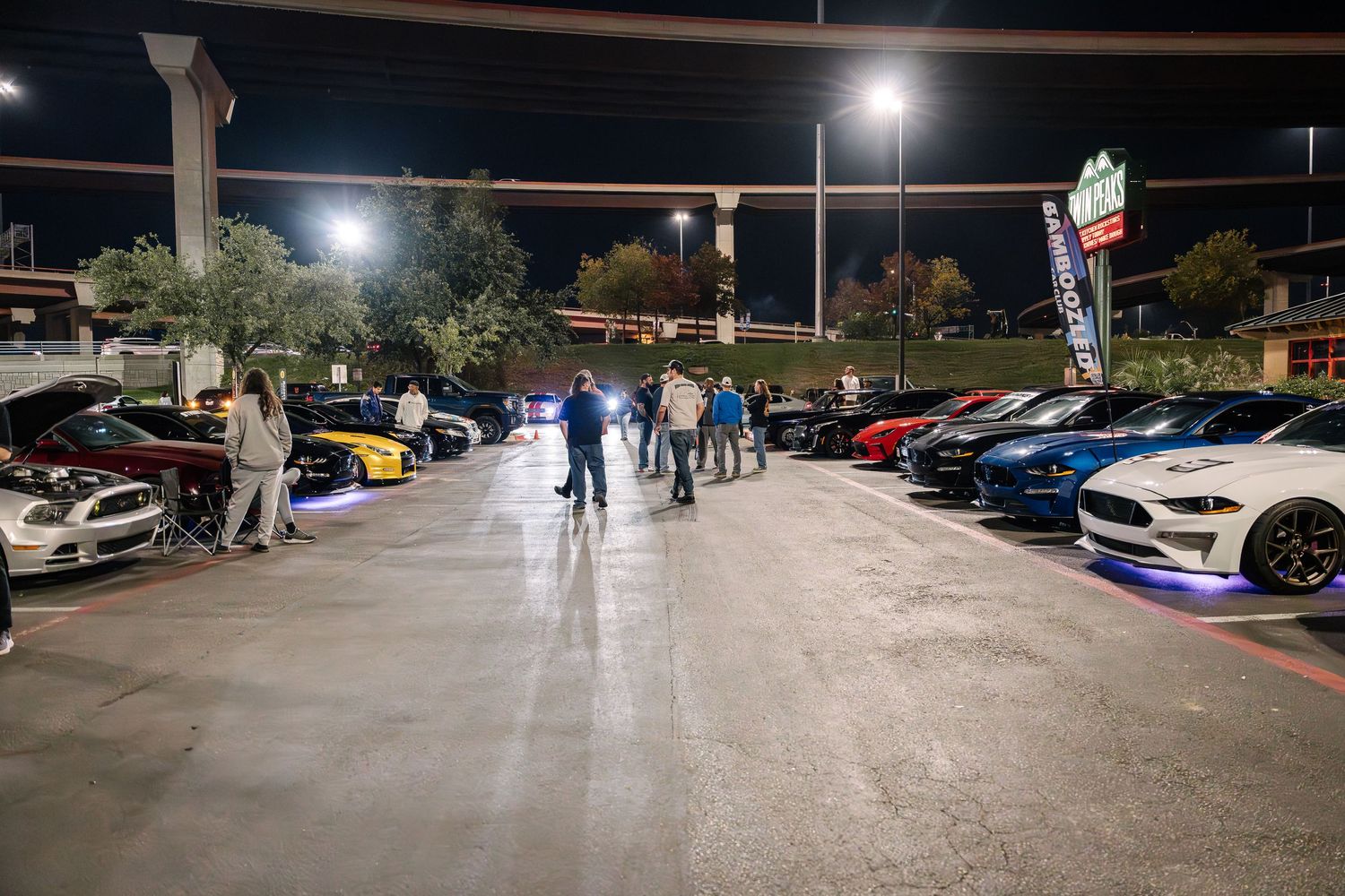 Car enthusiasts gather in a parking lot at night for a meet showcasing various performance vehicles.