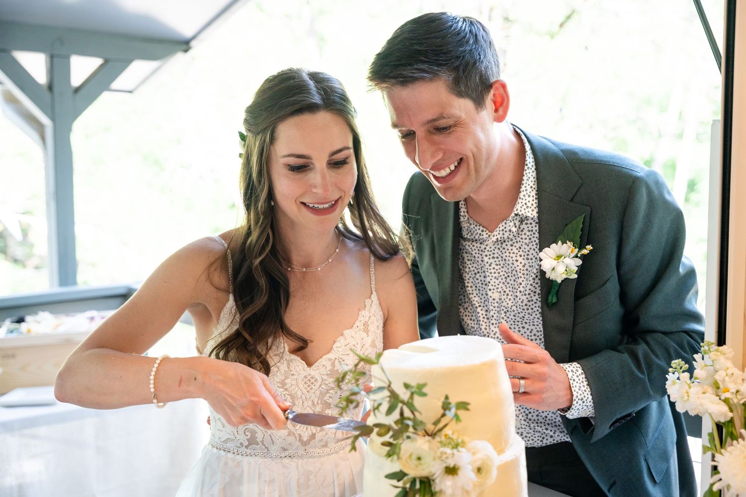 Joyful couple laughing while cutting their two-tier white wedding cake.