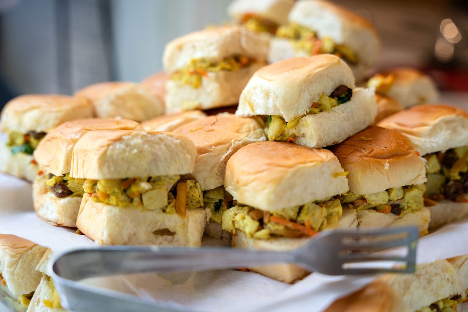Fresh slider sandwiches filled with egg salad stacked on a white serving platter.