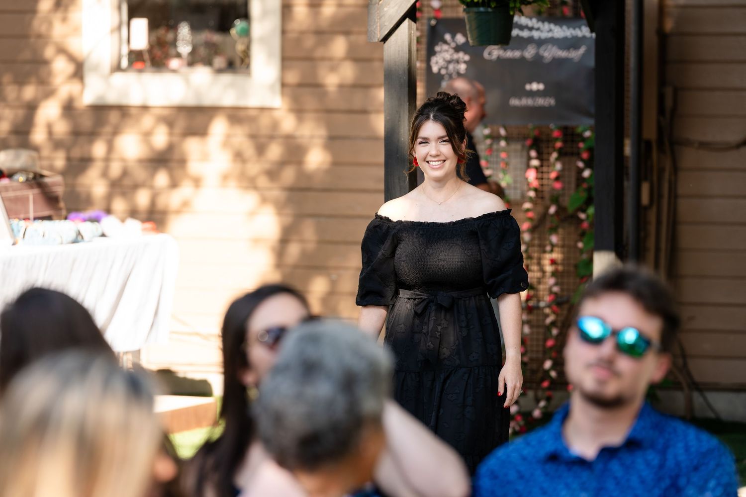 A gathering of wedding guests at an outdoor venue with string lights and wooden walls.