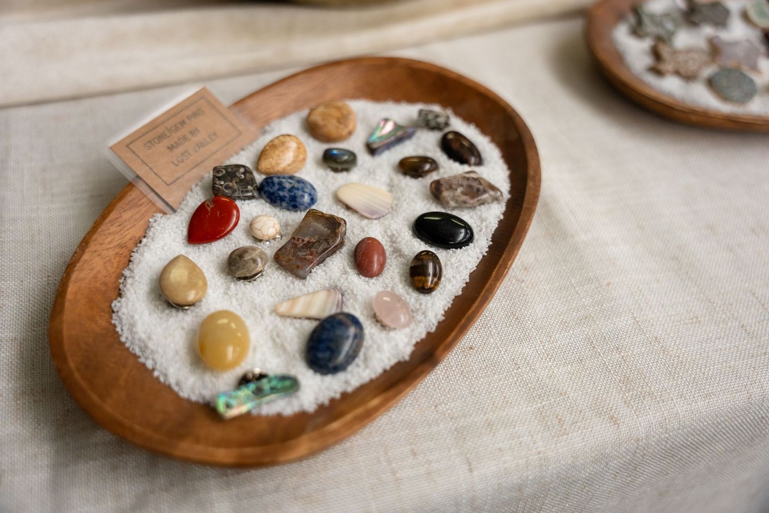 A wooden bowl filled with colorful polished stones and crystals displayed on a beige linen surface.