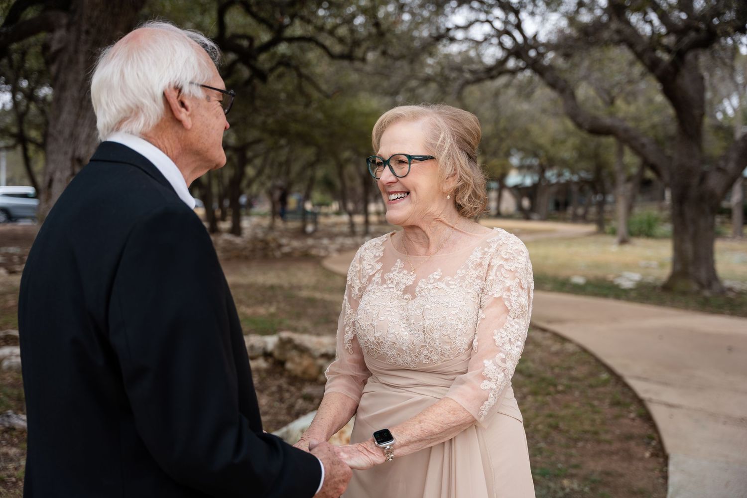 Elderly couple having an intimate moment together on a park path wearing formal attire.