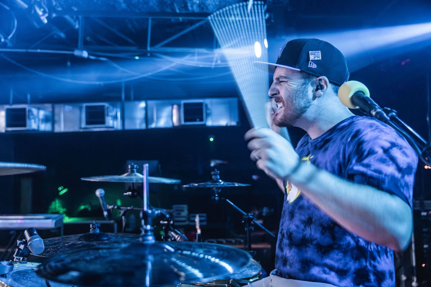 Drummer performing on stage with dramatic blue lighting and fog effects.