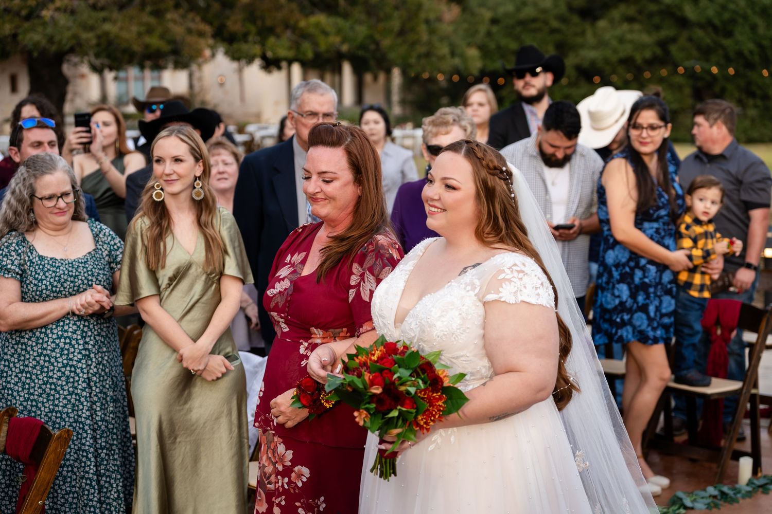 Wedding ceremony guests in colorful attire gather outdoors for a celebration.