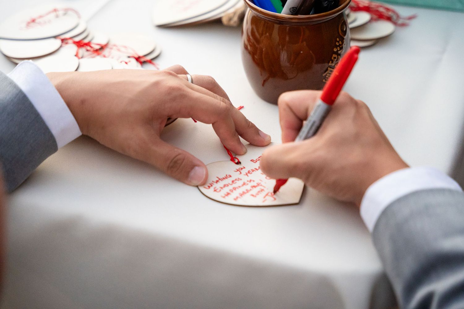 Hands writing message on paper heart at wedding guest book station.