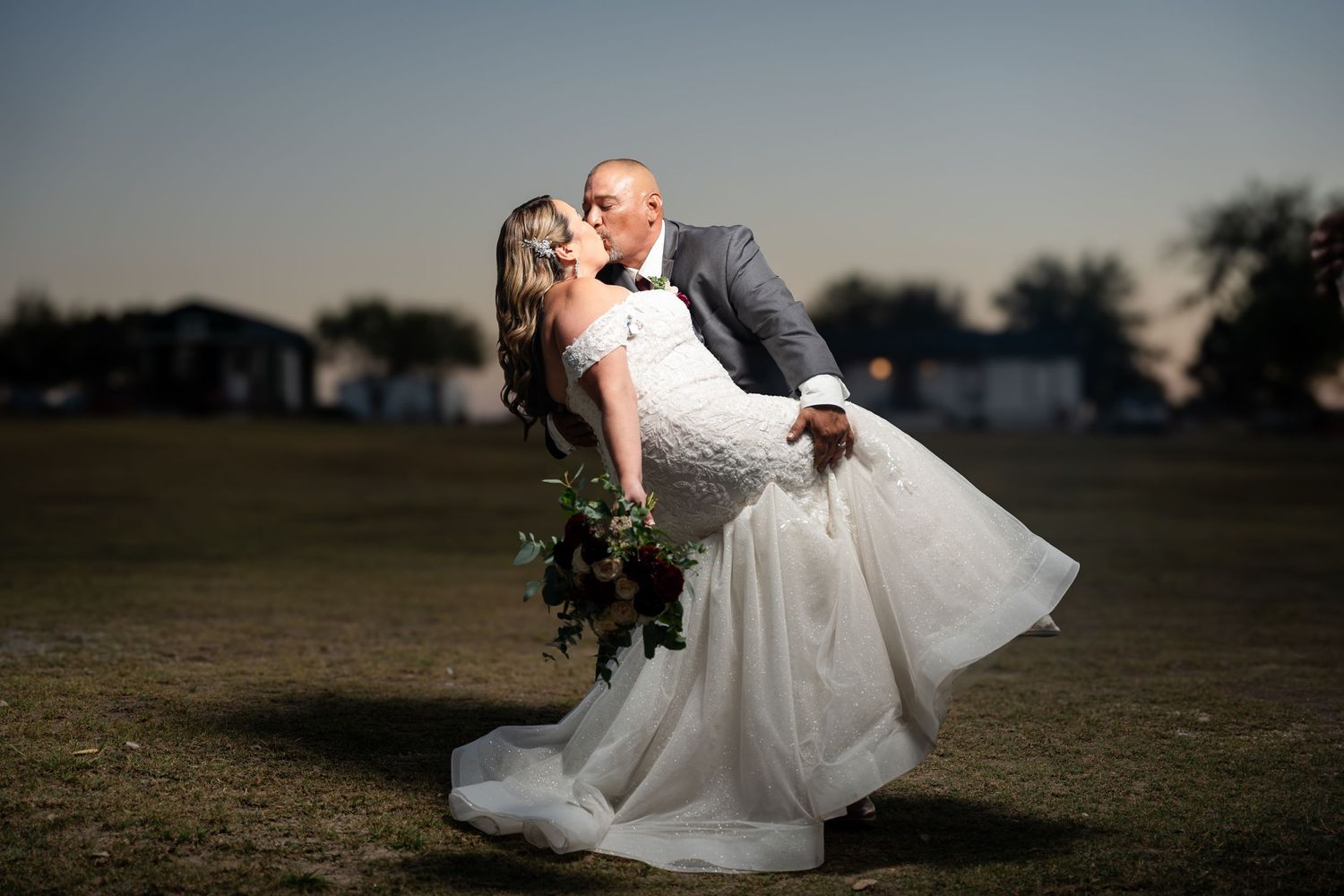 A romantic sunset dip pose between newlyweds in an outdoor field setting.