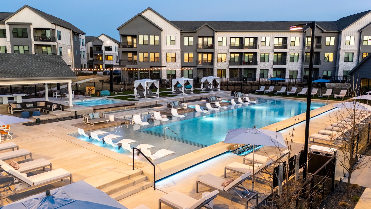 Modern luxury apartment complex with a large outdoor swimming pool surrounded by lounge chairs and landscaped grounds.