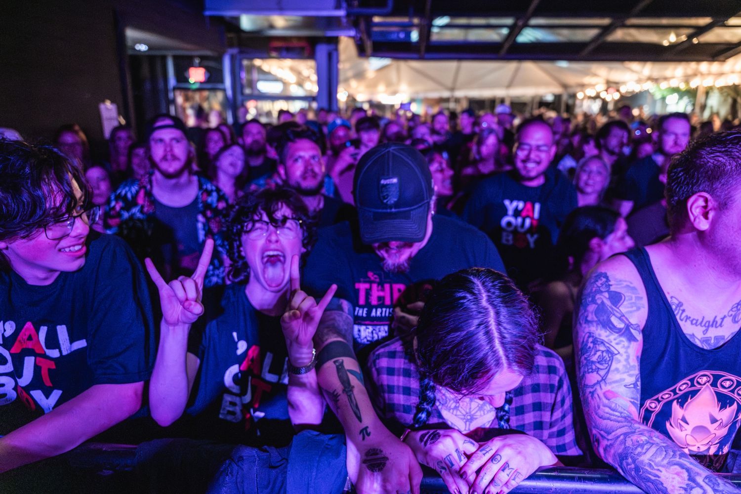 Enthusiastic crowd reacts to music performance in dark venue with purple lighting.