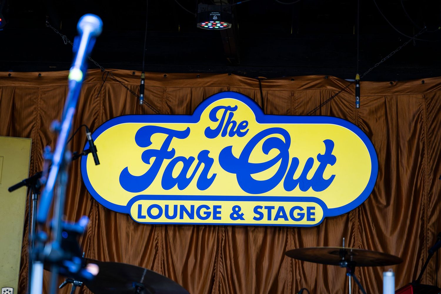 Illuminated vintage sign for The Far Out Lounge & Stage against a brown wood backdrop.