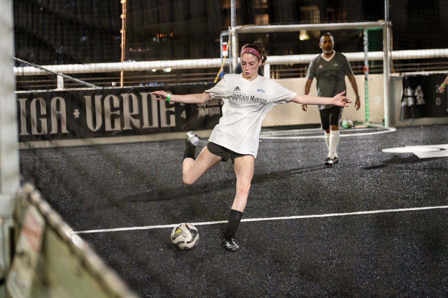 A player makes a dramatic kick during an indoor soccer match on a dark court.