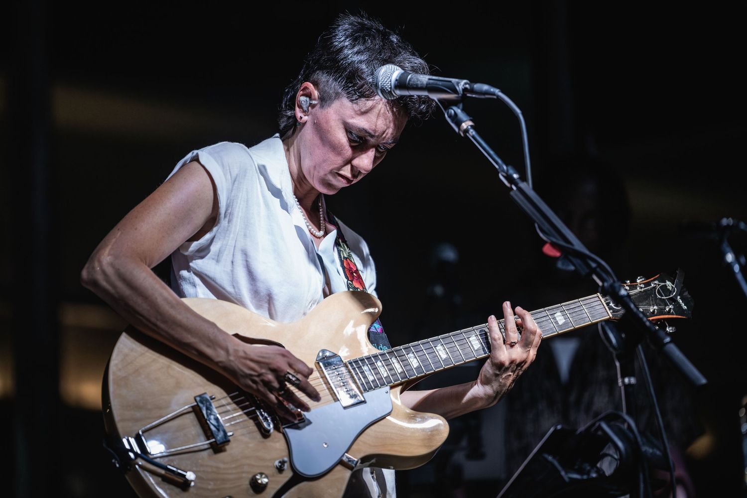 Guitarist playing an electric guitar while singing into a microphone on stage.